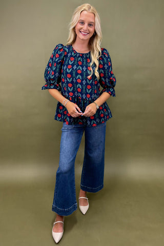Woman wearing a navy blue floral blouse and blue jeans against a green background