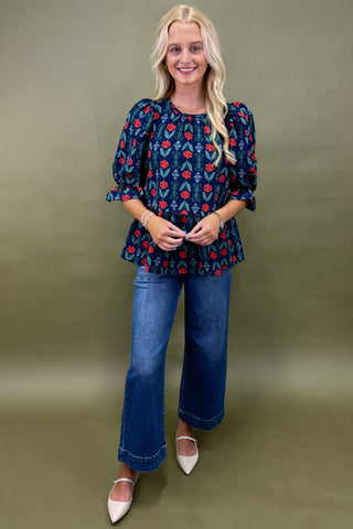 Woman wearing a blue floral blouse and jeans against a green background