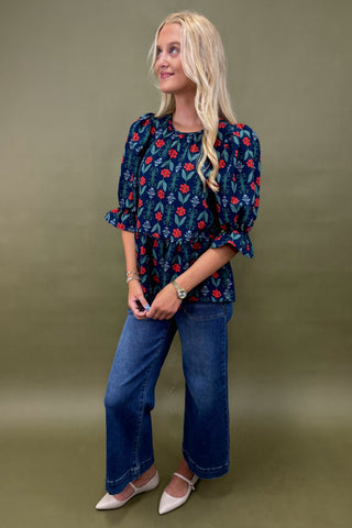 Woman wearing a blue floral blouse and jeans against a green background