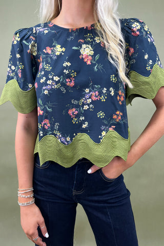 Woman wearing a floral blouse with green ruffled sleeves against a neutral background