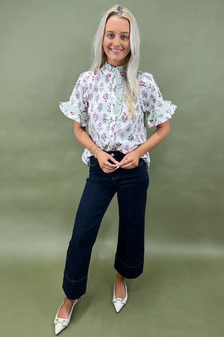 Woman wearing a floral blouse and dark jeans against a green background