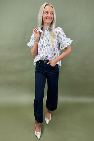 Woman wearing a floral blouse and dark jeans against a green background