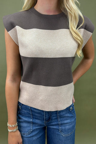 Woman wearing a sleeveless sweater with color-blocked design and blue jeans against a green background