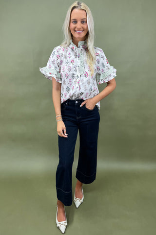 Woman wearing a floral blouse and dark jeans against a green background