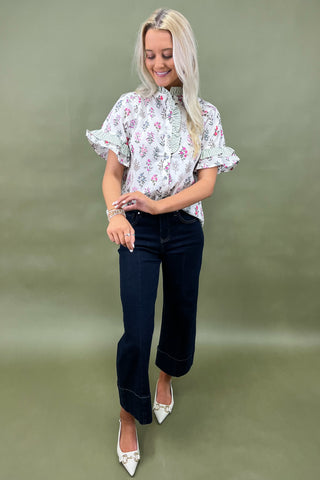 Woman wearing a floral blouse and dark jeans against a green background