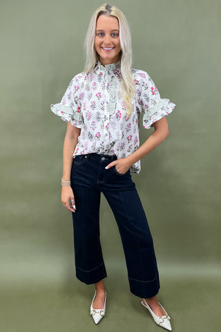 Woman wearing a floral blouse and dark jeans against a green background