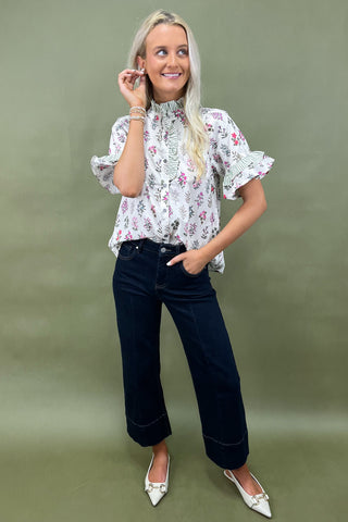 Woman wearing a floral blouse and dark jeans against a green background