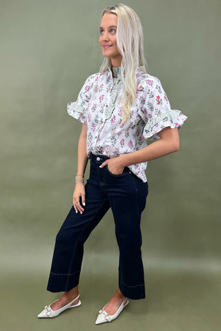 Woman wearing a floral blouse and dark pants against a green background