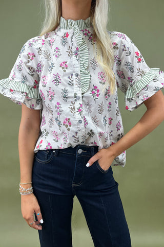 Woman wearing a floral blouse with ruffled sleeves against a green background
