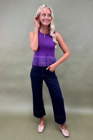 Woman wearing a purple top and dark blue jeans against a plain background