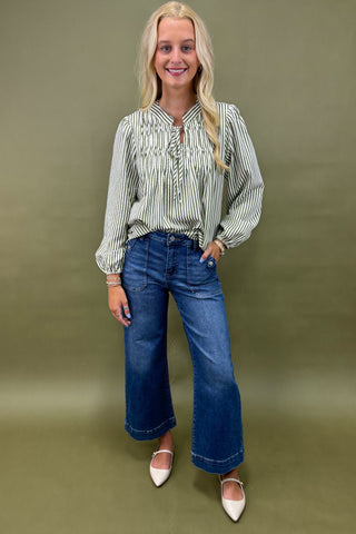 Woman wearing a striped shirt sage jean against a plain background