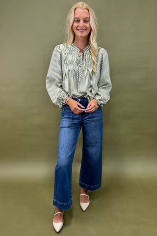Woman wearing a striped shirt and blue jeans against a green background