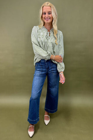 Woman wearing a striped shirt sage jean against a plain background
