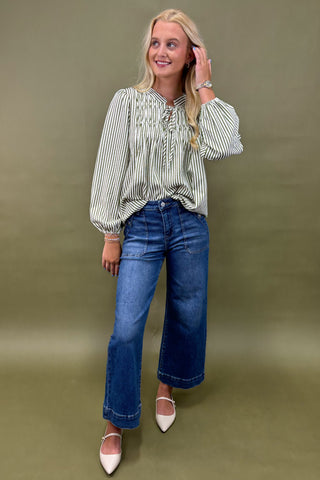 Woman wearing a striped shirt sage jean against a plain background