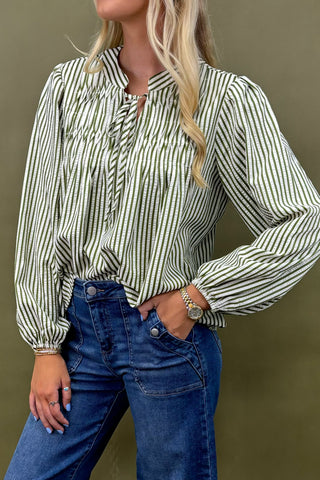 Woman wearing a green and white striped blouse with blue jeans against a brown background
