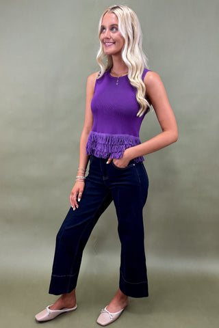 Woman wearing a purple top and dark blue jeans against a plain background