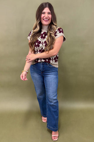 Woman wearing a floral top and blue jeans against a green background