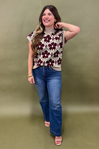 Woman wearing a floral top and blue jeans against a green background