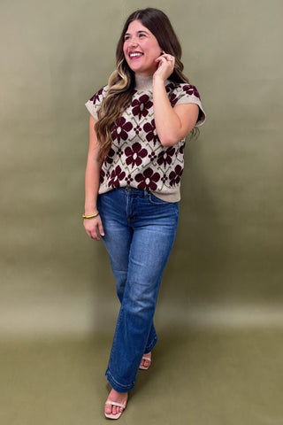 Woman wearing a floral top and blue jeans against a green background