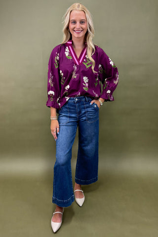 Woman wearing a purple floral blouse and blue jeans against a green background