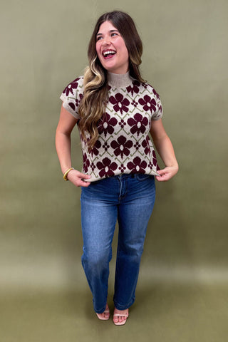 Woman wearing a patterned top and jeans against a plain background