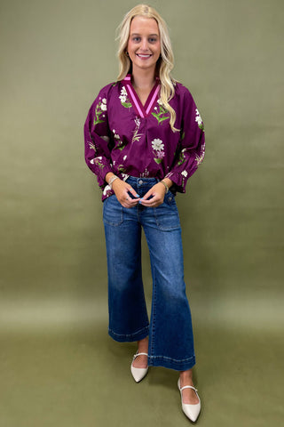 Woman wearing a purple floral blouse and blue jeans against a green background