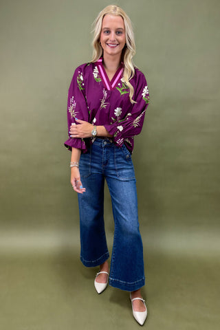 Woman wearing a purple floral blouse and blue jeans against a green background
