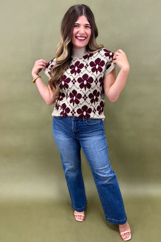 Woman wearing a patterned sleeveless top and blue jeans against a green background