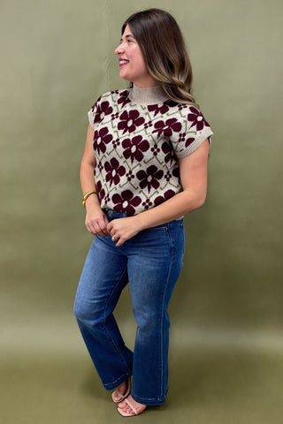 Woman wearing a patterned top and blue jeans against a green background