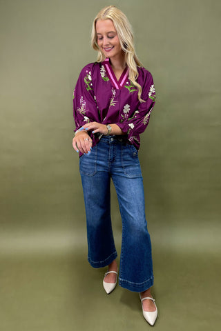 Woman wearing a purple floral blouse and blue jeans on a green background