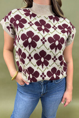 Person wearing a short-sleeve sweater with a floral pattern against a plain background