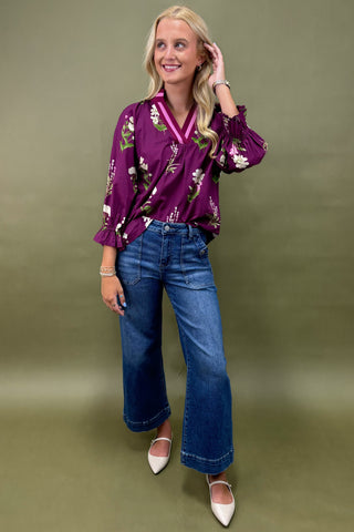 Woman wearing a purple floral blouse and blue jeans against a green background