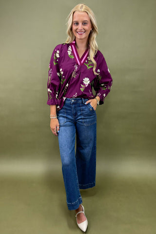 Woman wearing a purple floral blouse and blue jeans against a green background