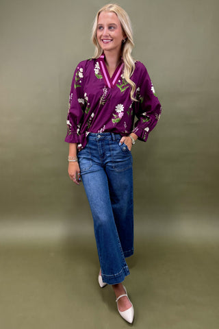 Woman wearing a purple floral blouse and blue jeans against a green background