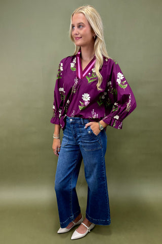 Woman wearing a purple floral blouse and blue jeans against a green background