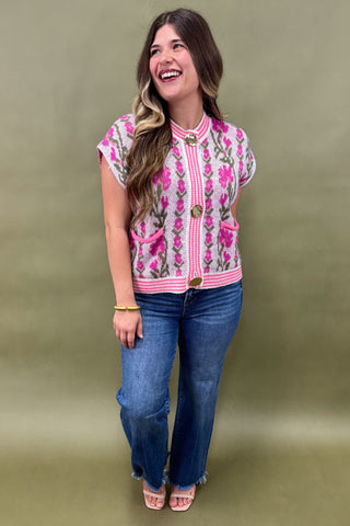 Woman wearing a pink floral embroidered top and blue jeans against a green background