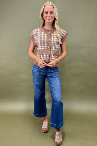 Woman wearing a patterned vest and blue jeans against a green background