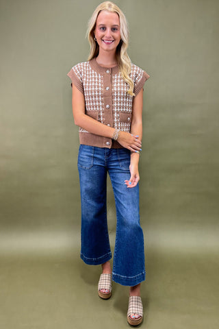 Woman wearing a patterned top and blue jeans against a green background