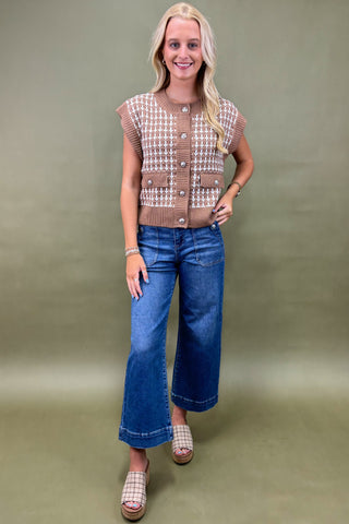 Woman wearing a patterned short-sleeve top and blue jeans against a plain background