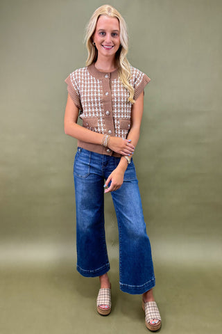 Woman wearing a patterned top and blue jeans against a green background