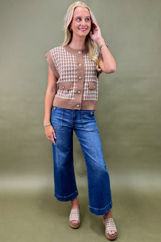 Woman wearing a patterned vest and blue jeans against a green background