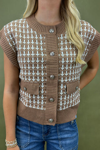 Person wearing a brown and white patterned vest with buttons on a green background