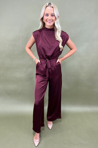 Woman wearing a burgundy jumpsuit on a plain background