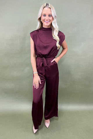 Woman wearing a burgundy jumpsuit on a plain background