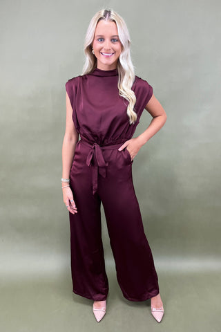 Woman wearing a maroon jumpsuit against a plain background