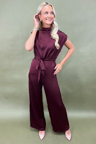 Woman wearing a burgundy jumpsuit against a green background