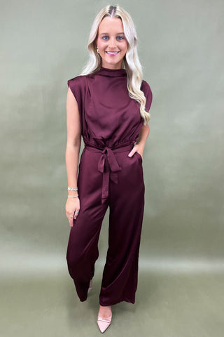 Woman wearing a burgundy jumpsuit against a plain background