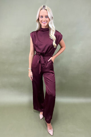Woman wearing a burgundy jumpsuit against a plain background