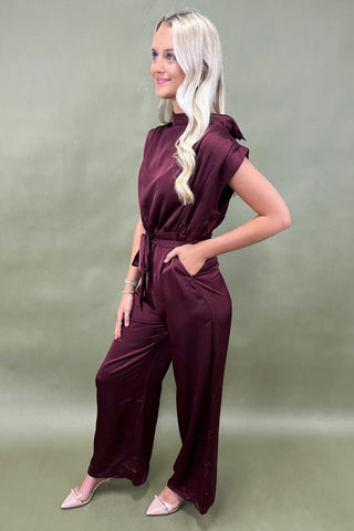 Woman wearing a burgundy jumpsuit against a plain background
