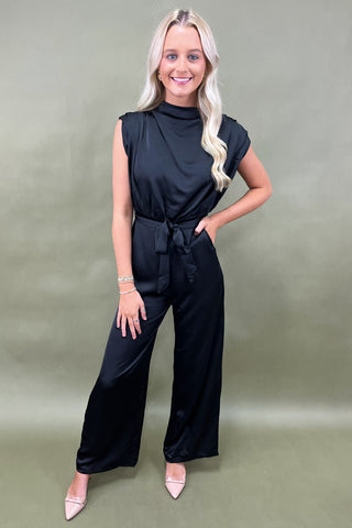 Woman wearing a black sleeveless jumpsuit on a green background